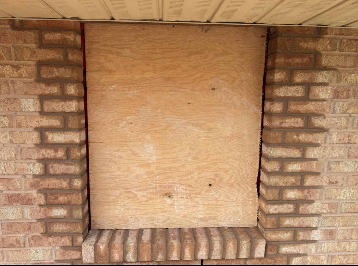 Window opening in a brick wall boarded up with a brick sill below